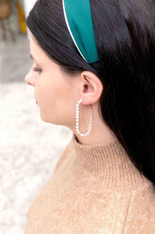 Beaded Racetrack Hoop Earrings featuring gold wire and accented with emerald green beads, displayed on a white surface.