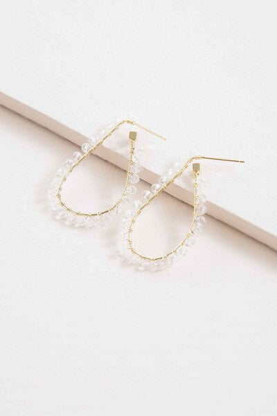 The Delicate Drops Hoop Earrings, featuring gold teardrop designs with pearl accents and clear beads, are displayed on a white surface.