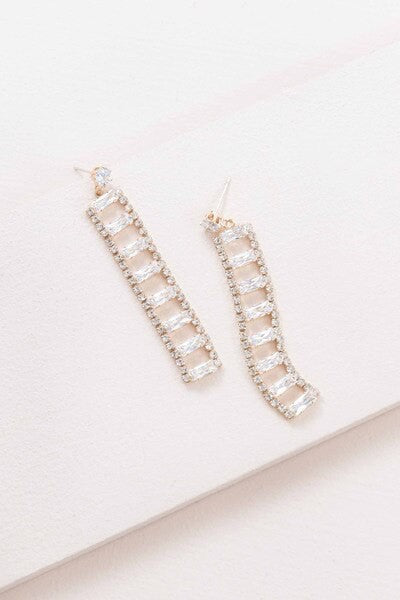 A Dozen Diamonds Dangle Earrings on a pale pink background.