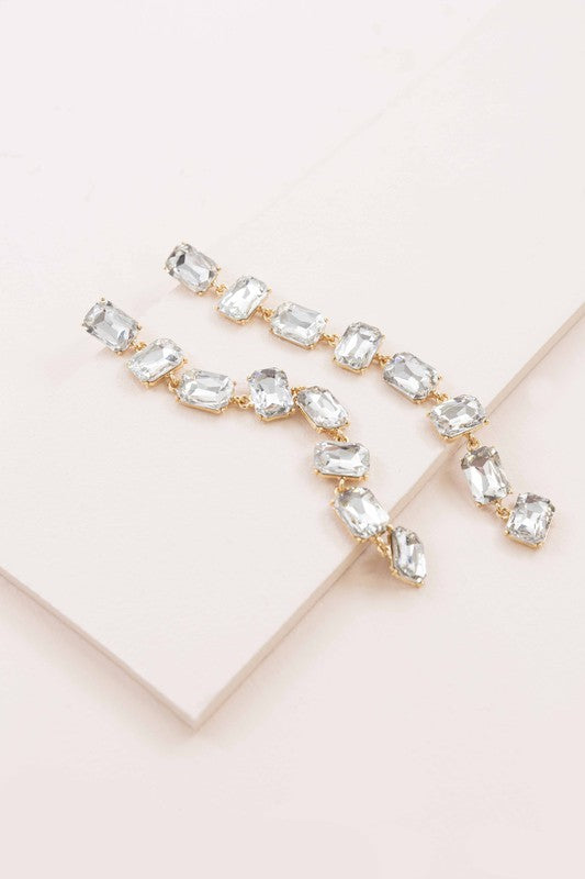 More Drama Dangle Earrings with clear rectangular diamond stones on a pastel pink background, perfect for formal occasions.