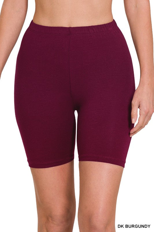 A person is wearing burgundy-colored, fitted Premium Cotton Biker Shorts that reach mid-thigh. The activewear shorts have an elastic waistband and are made from high-quality cotton.