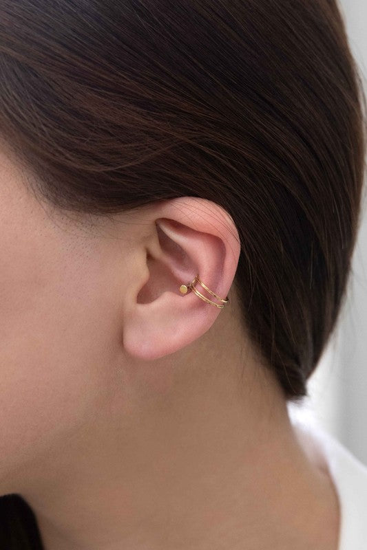 This minimalist jewelry piece, aptly named "Double the Gold Ear Cuff," is crafted from 14K gold over stainless steel and showcases a sleek double band design. Elegantly placed on a white surface, it embodies the simple sophistication of a golden open cuff ring.