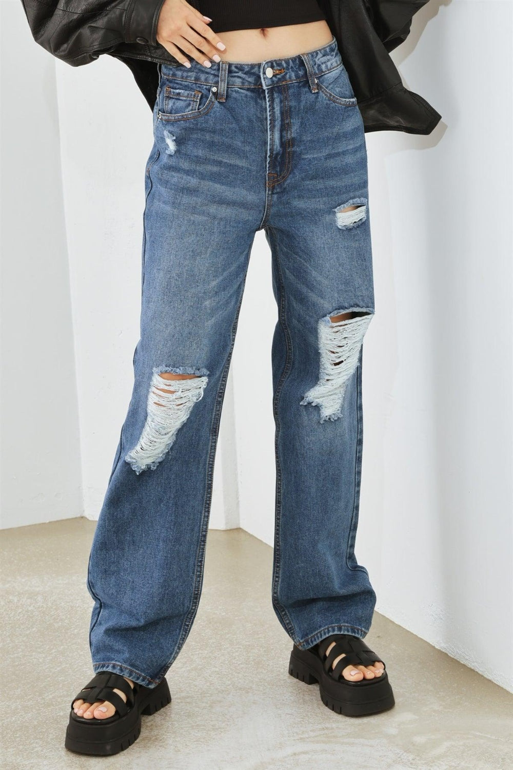 Person wearing HAMMER COLLECTION Distressed High Waist Jeans with ripped knees and black platform sandals, standing in a minimalist setting. The flattering fit and edgy distressed details add to the overall chic look.