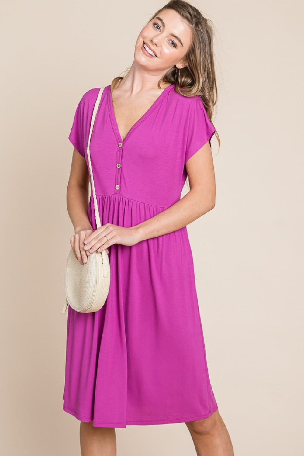 A person stands against a neutral background wearing the BOMBOM V-Neck Short Sleeve Dress, featuring a vibrant pink color and button details, crafted from soft rayon spandex fabric.