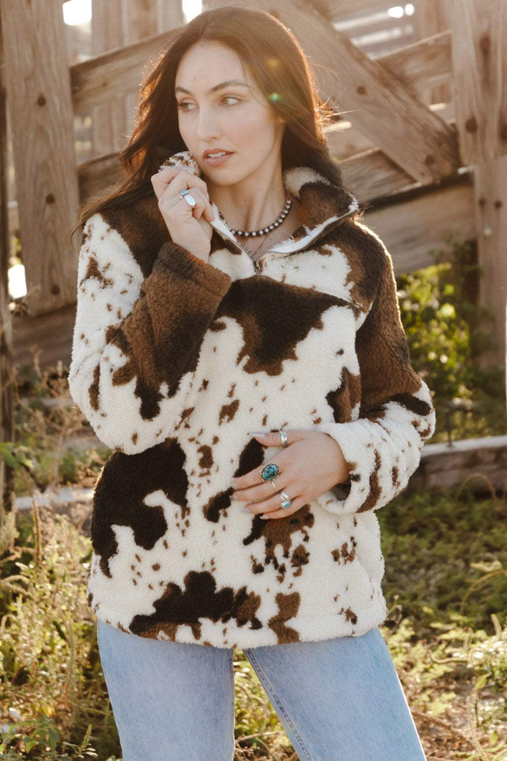 A person wearing a Zip Collar Cow Print Fleece Sweatshirt and light blue jeans stands outdoors with their back to the camera, showcasing the skin-friendly fleece material.