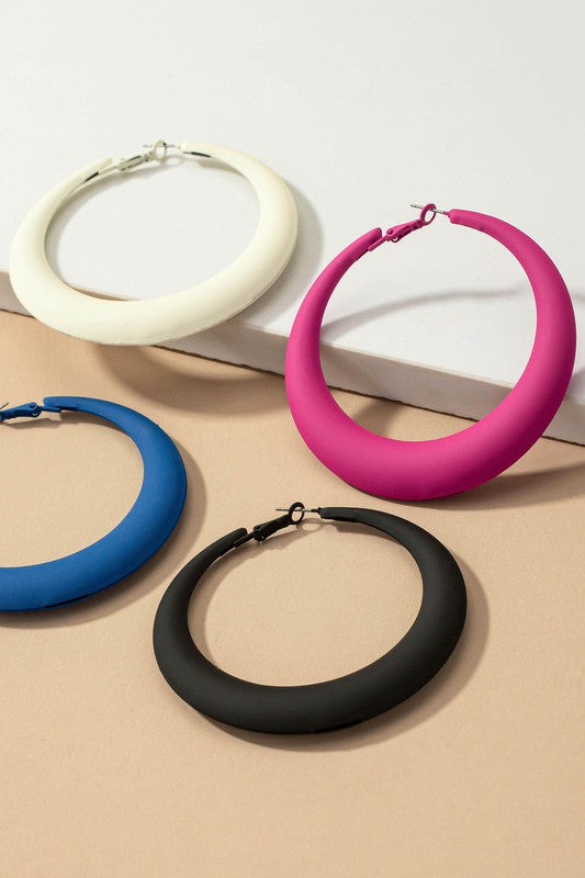 Four large color coated puffy hoop earrings, available in off-white, pink, blue, and black hues, are neatly displayed on a beige surface and white platform.