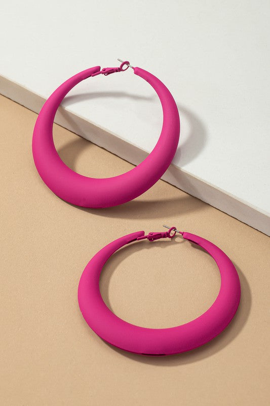 Four large color coated puffy hoop earrings, available in off-white, pink, blue, and black hues, are neatly displayed on a beige surface and white platform.