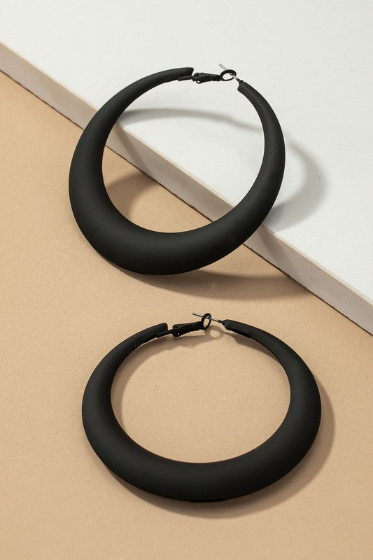 Four large color coated puffy hoop earrings, available in off-white, pink, blue, and black hues, are neatly displayed on a beige surface and white platform.