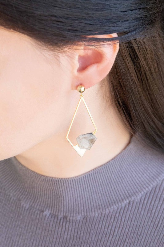 Introducing the Marble Drop Earrings, which showcase an asymmetric geometric design with mismatched elements: one earring features a large stone and triangle with 14k gold-plated accents, while the other earring includes a hexagon and small bead.