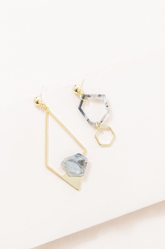 Introducing the Marble Drop Earrings, which showcase an asymmetric geometric design with mismatched elements: one earring features a large stone and triangle with 14k gold-plated accents, while the other earring includes a hexagon and small bead.