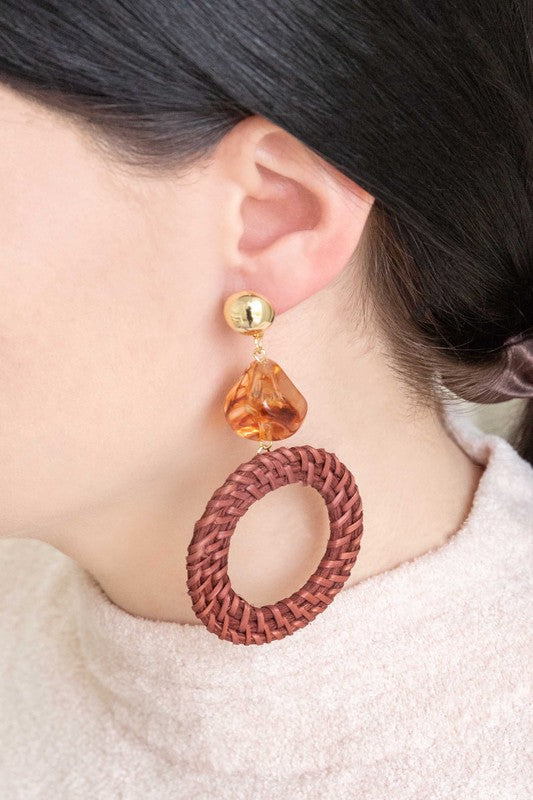 The Wicker and Amber Drop Earrings are beautifully designed with intricately woven wicker combined with amber beads and gold accents, all set against a white backdrop to add an elegant touch.