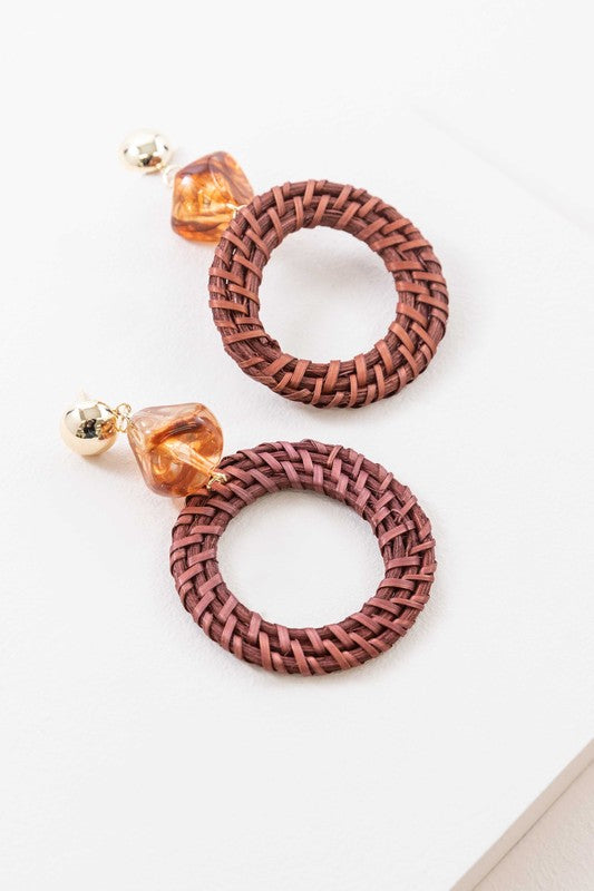 The Wicker and Amber Drop Earrings are beautifully designed with intricately woven wicker combined with amber beads and gold accents, all set against a white backdrop to add an elegant touch.