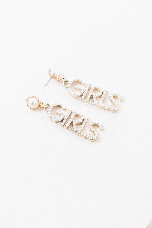 A pair of One of The Girls Drop Earrings with the word "girls" spelled out in gemstones on a white background.