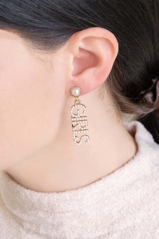 A pair of One of The Girls Drop Earrings with the word "girls" spelled out in gemstones on a white background.