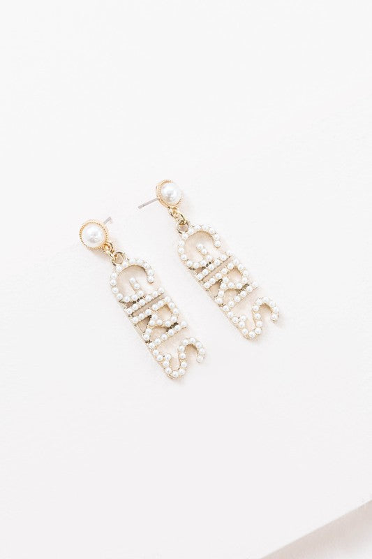A pair of One of The Girls Drop Earrings with the word "girls" spelled out in gemstones on a white background.