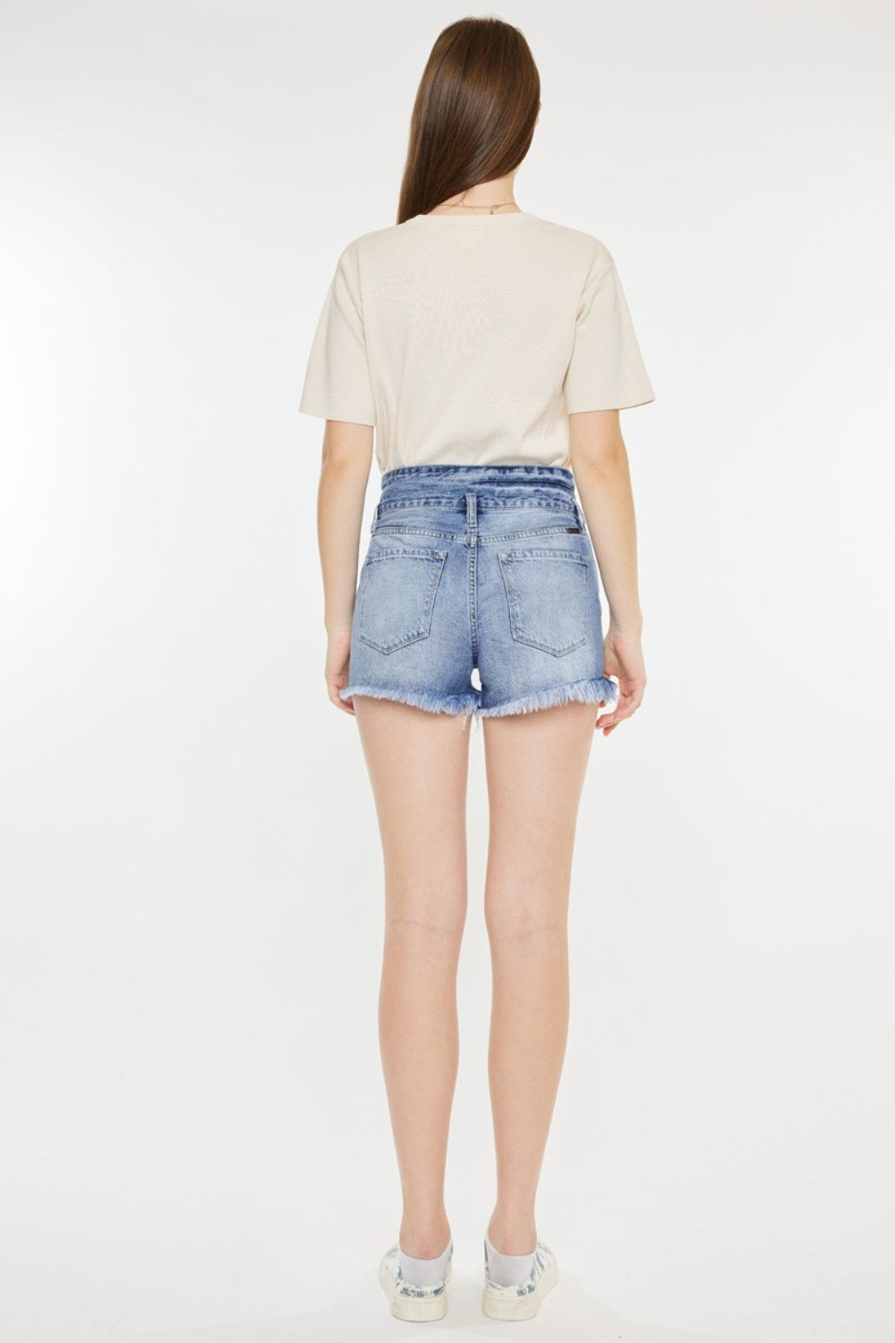 A person wearing a beige t-shirt and Kancan High Rise Frayed Hem Denim Shorts, paired with patterned sneakers, stands against a white background—an ideal addition to any summer wardrobe.