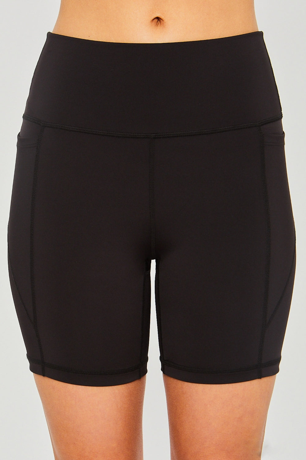 A person wearing Love Tree High Waist Seam Detail Active Shorts in black, casually resting their hands in the pockets against a plain background.