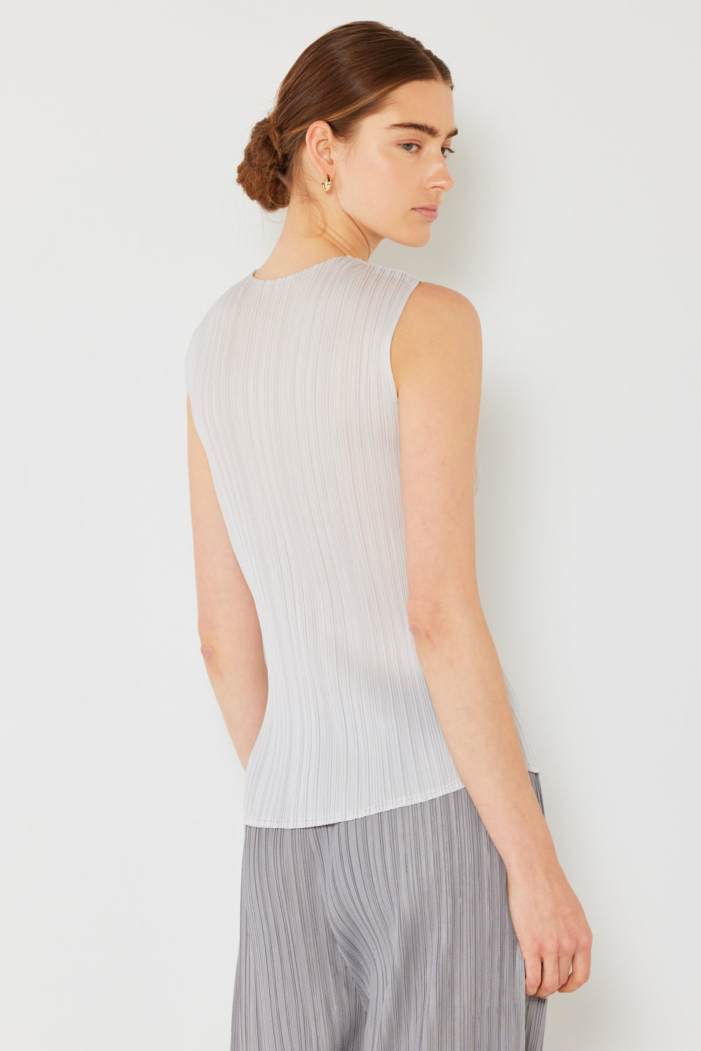 Person wearing a Marina West Swim Pleated Sleeveless Crewneck Tank and a gray pleated skirt, standing against a white background.