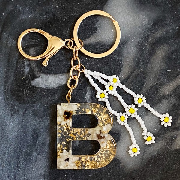 Baby Daisy Initial Key Chain alphabet keychains with real daisy flowers and gold flakes on a marble surface.