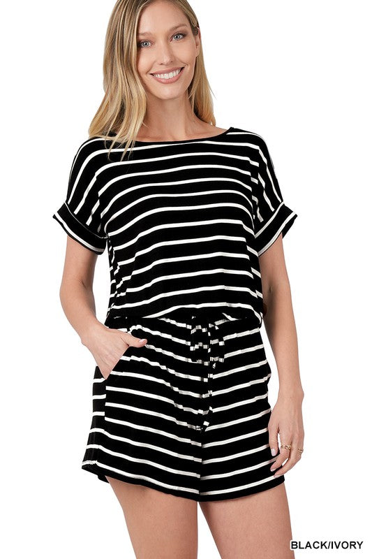 A person is smiling while wearing the Stripe Romper with Pockets, featuring a chic design and an elastic waist, with hands casually placed in the pockets.