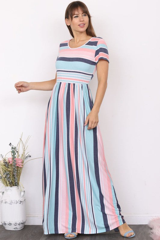 A woman wearing a Short Sleeve Stripe Maxi Dress leans against a plain white wall, casually placing her hand in her pocket.