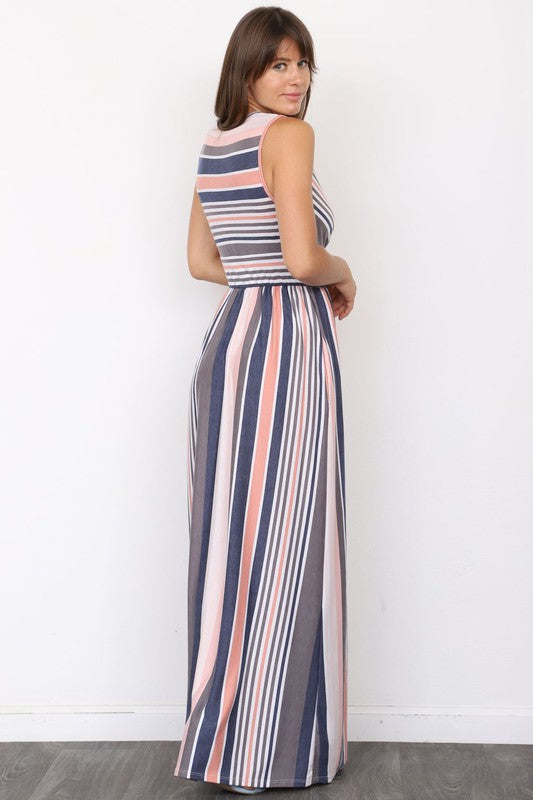 A person wearing the elegant Surplice Stripe Maxi Dress adorned with vertical pastel stripes in blue, pink, and white, stands gracefully on a wooden floor.