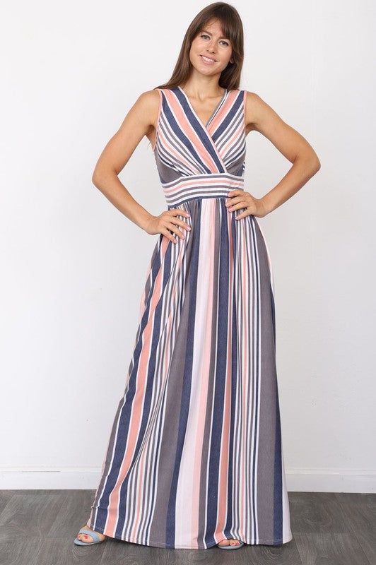 A person wearing the elegant Surplice Stripe Maxi Dress adorned with vertical pastel stripes in blue, pink, and white, stands gracefully on a wooden floor.