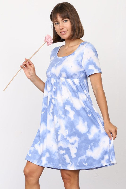 A person in a stylish Cloud Tie Dye Midi Dress made from smooth polyester, paired with black sandals, stands on a light-colored floor in front of a beige curtain backdrop.