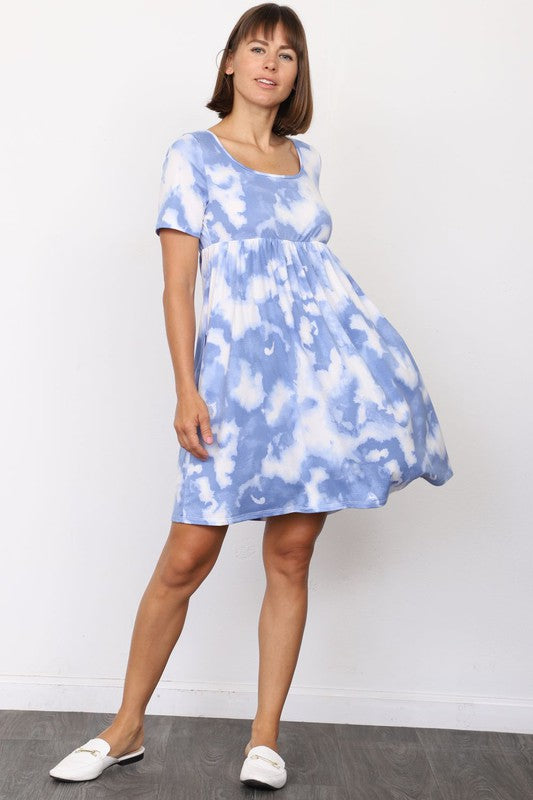 A person in a stylish Cloud Tie Dye Midi Dress made from smooth polyester, paired with black sandals, stands on a light-colored floor in front of a beige curtain backdrop.