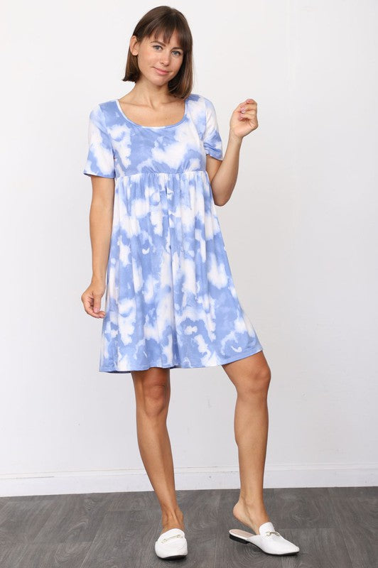 A person in a stylish Cloud Tie Dye Midi Dress made from smooth polyester, paired with black sandals, stands on a light-colored floor in front of a beige curtain backdrop.