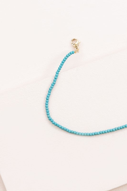 The Turquoise Beaded Anklet, featuring a delicate gold-plated chain and clasp, is elegantly showcased on a white surface.