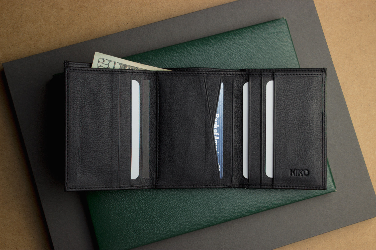 A Trifold Wallet made from full grain cowhide leather holds cash, a card, and has a visible ID section on top of a closed red notebook.