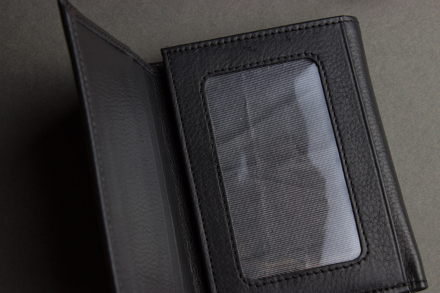 A Trifold Wallet made from full grain cowhide leather holds cash, a card, and has a visible ID section on top of a closed red notebook.