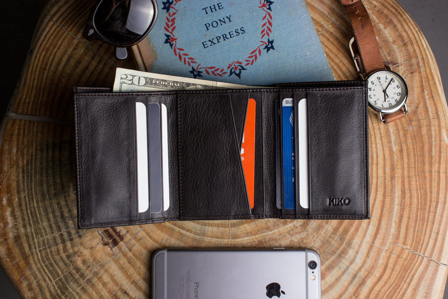 A Trifold Wallet made from full grain cowhide leather holds cash, a card, and has a visible ID section on top of a closed red notebook.