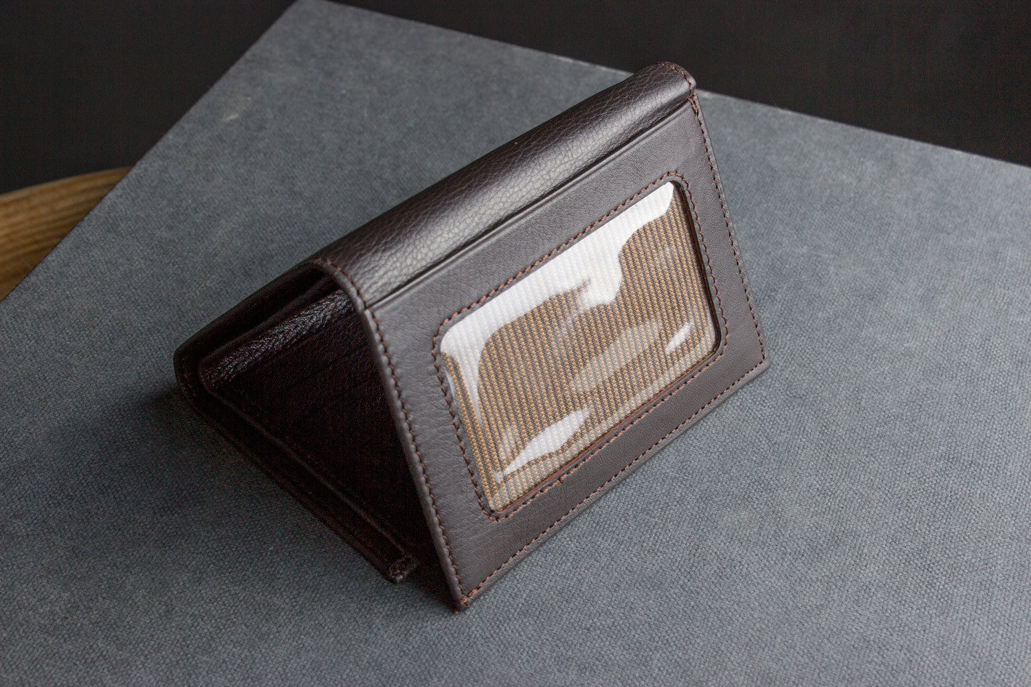 A Trifold Wallet made from full grain cowhide leather holds cash, a card, and has a visible ID section on top of a closed red notebook.