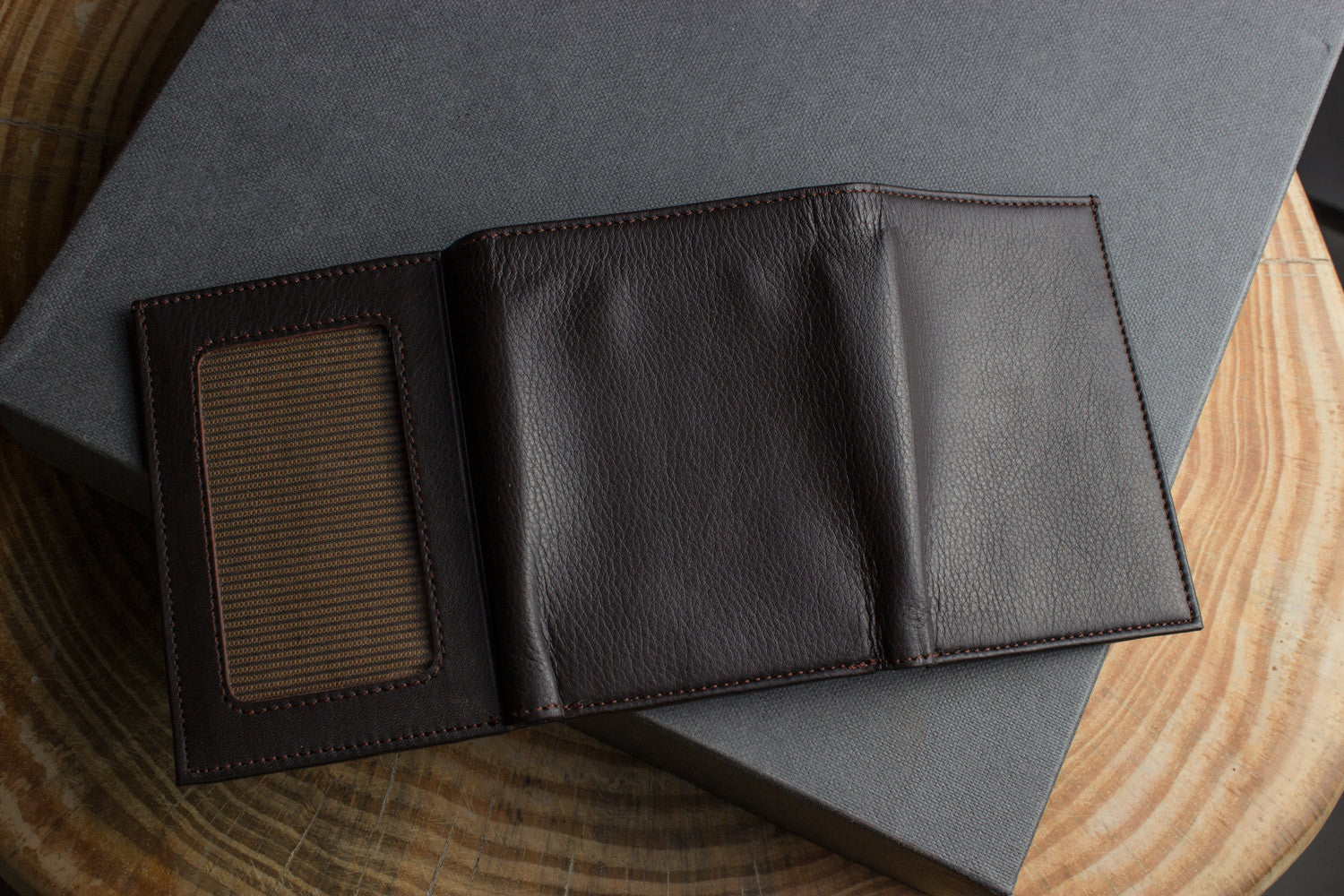 A Trifold Wallet made from full grain cowhide leather holds cash, a card, and has a visible ID section on top of a closed red notebook.