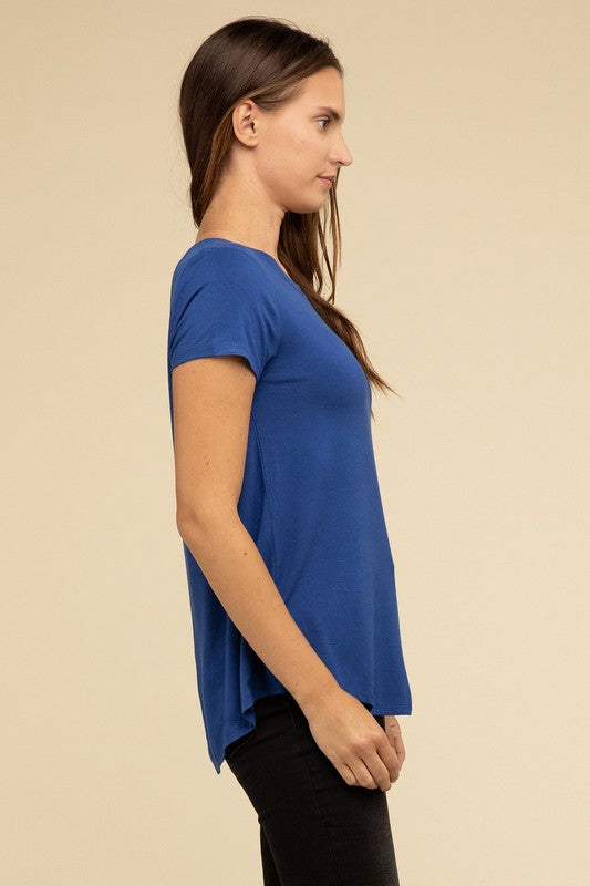 A person with long hair is wearing a blue Flowy Round Hem Rayon Short Sleeve Top and black pants, standing against a plain beige background.