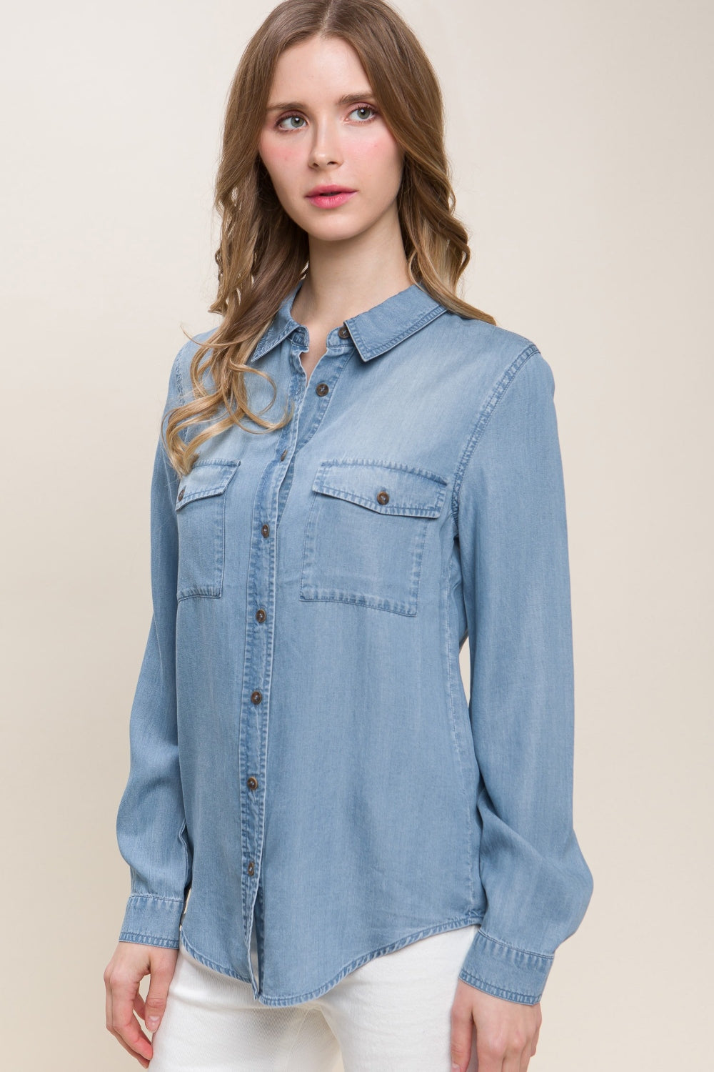 A woman in a Love Tree Scooped Hem Button Up Denim Shirt paired with white pants stands against a neutral background.