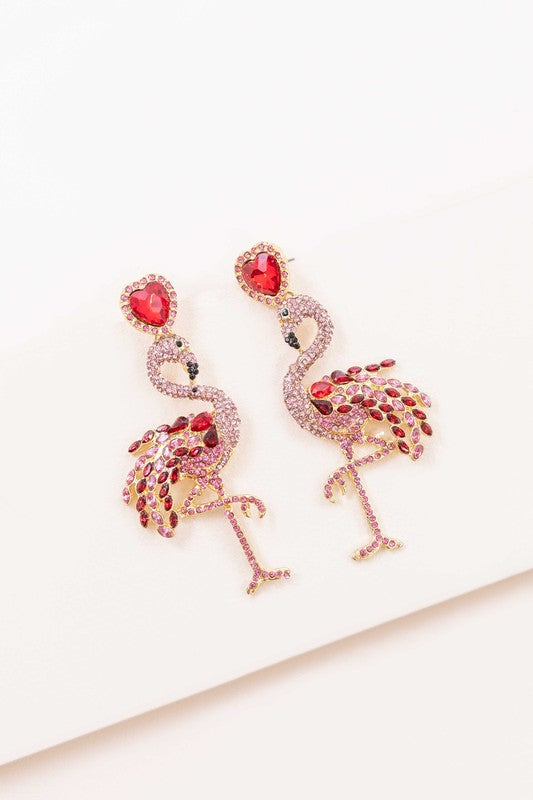 The Pink Flamingo Drop Earrings, featuring pink rhinestones and heart-shaped red studs with jeweled accents, add a charming flair of summer style against a white background.