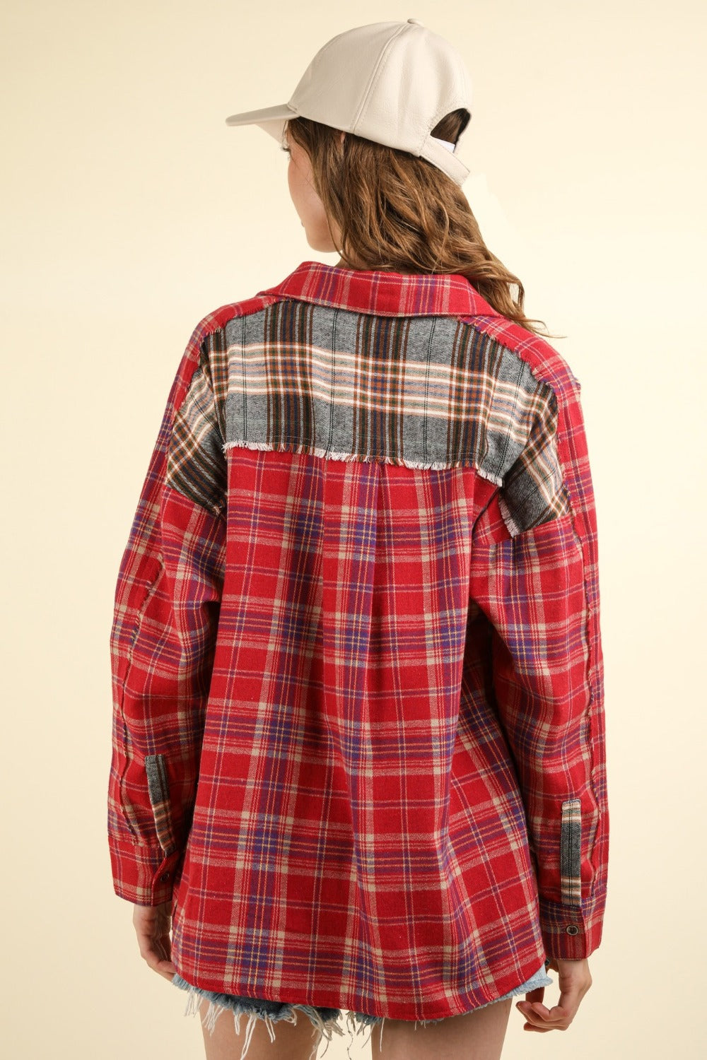 A woman wearing a VERY J Contrast Plaid Raw Detail Shirt, blue denim shorts, and a beige cap poses against a plain background.