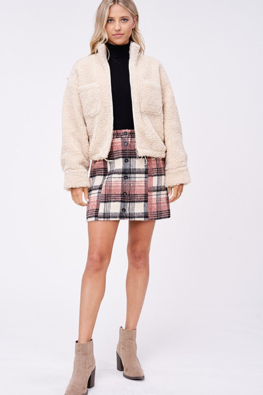 Model wears size small SHERPA JACKET WITH FRONT POCKETS in beige, a black turtleneck, and a pink plaid button-up skirt made of imported polyester, standing against a plain white background.