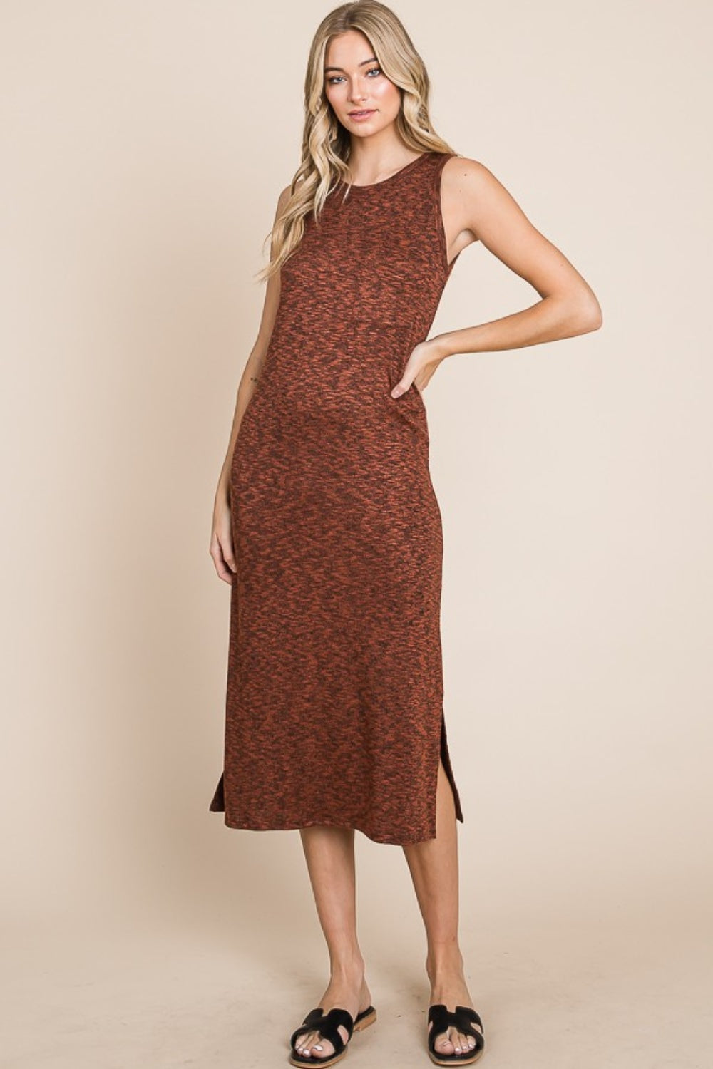 A woman with long blonde hair stands against a beige background, wearing the versatile and stylish BOMBOM Slit Round Neck Sleeveless Midi Dress in rust color, featuring a slit round neck and side slit, paired with black sandals.