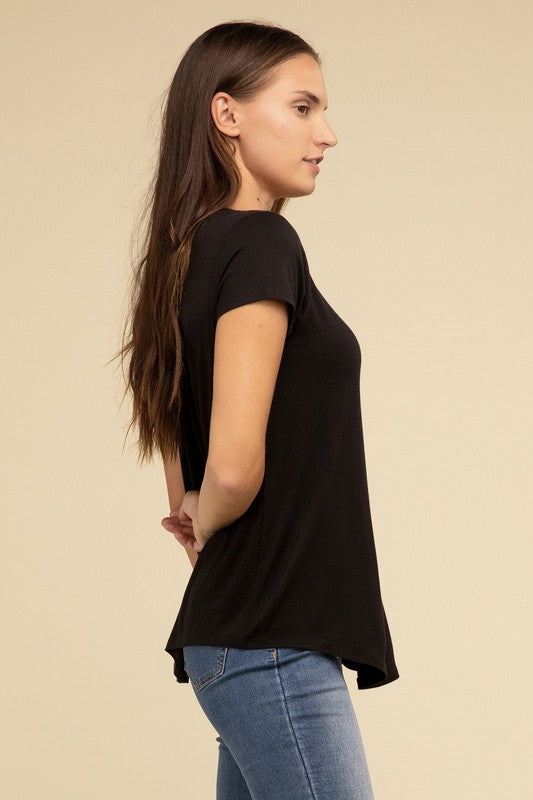 A person with long hair is wearing a blue Flowy Round Hem Rayon Short Sleeve Top and black pants, standing against a plain beige background.