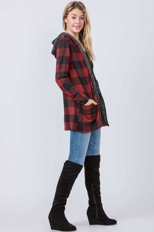 A woman wearing a Buffalo Plaid Hooded Cardigan and patterned pants stands against a white paneled background. Made in the United States.