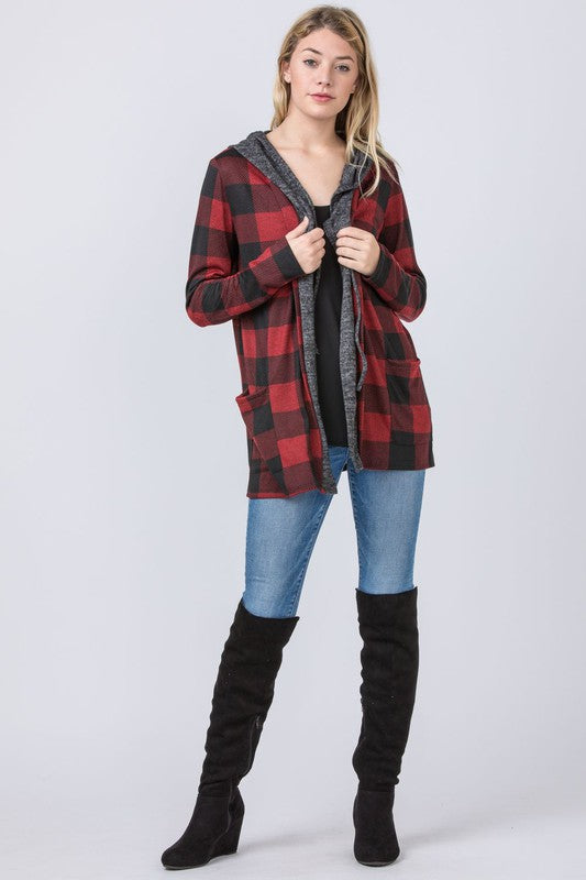 A woman wearing a Buffalo Plaid Hooded Cardigan and patterned pants stands against a white paneled background. Made in the United States.