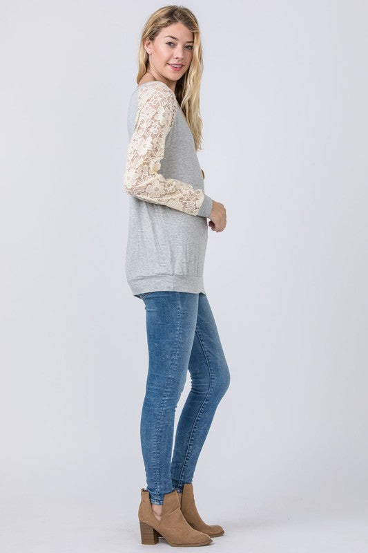 A person in a Plus Lace Sleeve Raglan Tunic, dark jeans, and black heels stands against a plain background.