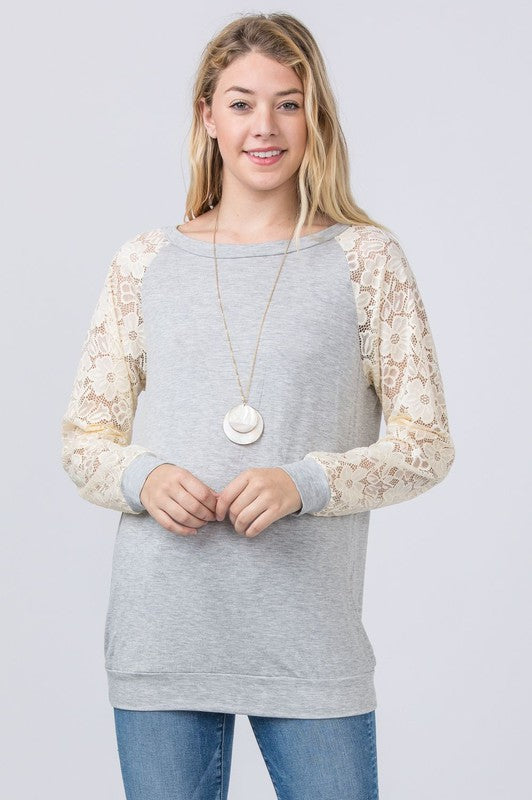 Dressed in a Lace Sleeve Raglan Tunic made from soft rayon spandex fabric, a woman poses elegantly against a plain background, pairing the tunic effortlessly with dark jeans. Made in the United States, her outfit beautifully combines comfort and style.