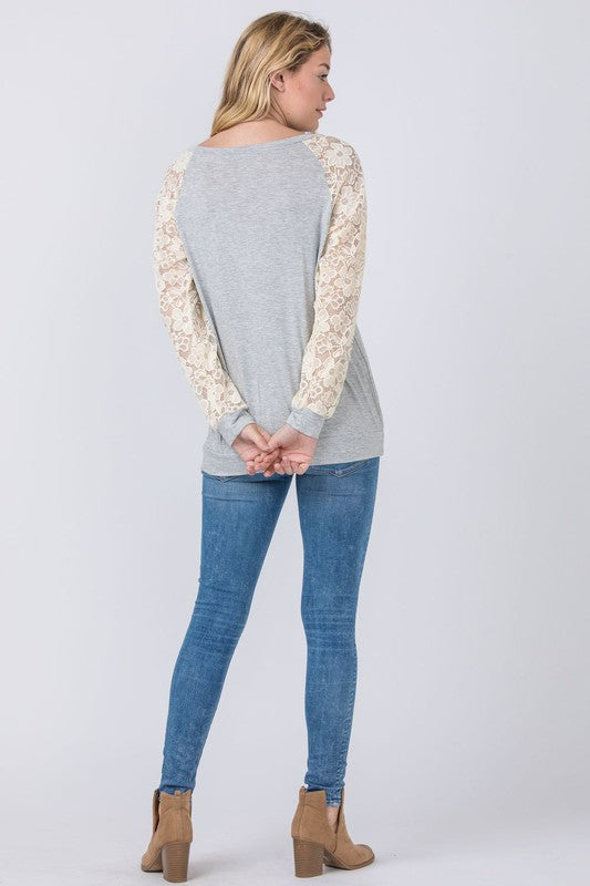 Dressed in a Lace Sleeve Raglan Tunic made from soft rayon spandex fabric, a woman poses elegantly against a plain background, pairing the tunic effortlessly with dark jeans. Made in the United States, her outfit beautifully combines comfort and style.