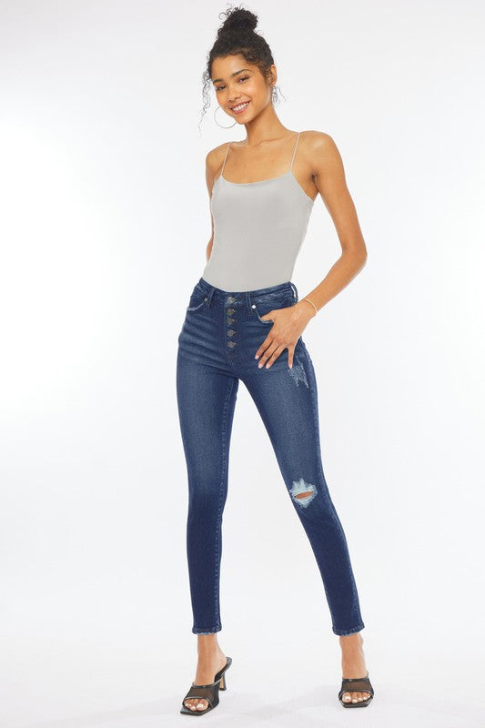 A woman in a gray tank top and High Rise Piecing Detail Super Skinny Jeans stands against a plain white backdrop while looking down and smiling. She is wearing black heeled sandals.