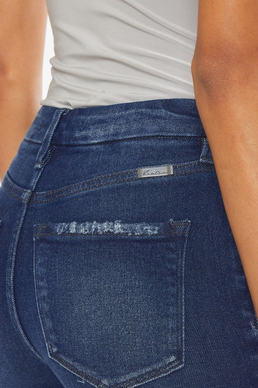 A woman with curly hair wearing a grey tank top, High Rise Piecing Detail Super Skinny Jeans with button closure, and black heeled sandals stands against a plain white background.